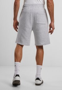 Grå bomullsblandingsshorts med elastisk midje og en enkelt baklomme. Brukt med hvite sokker og svart-hvite joggesko.