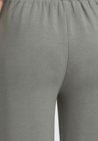 Szürke leggings, rugalmas derékkal, sima textúrával és testhezálló dizájnnal, ami kiemeli a lábak kontúrjait. Nincsenek minták vagy díszítések.