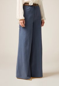 Weite Denim-Hosen in Hellblau, mit hohem Bund und subtiler Textur. Kombiniert mit einem braunen Gürtel, ergänzt durch ein beiges Oberteil.