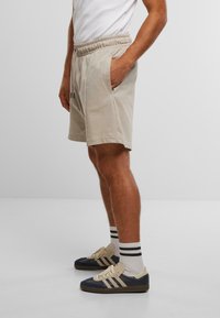 Beige Shorts mit einem elastischen Bund, seitlichen Taschen und einem lässigen Schnitt. Kombiniert mit marineblauen und beigen Sneakers sowie gestreiften Socken.