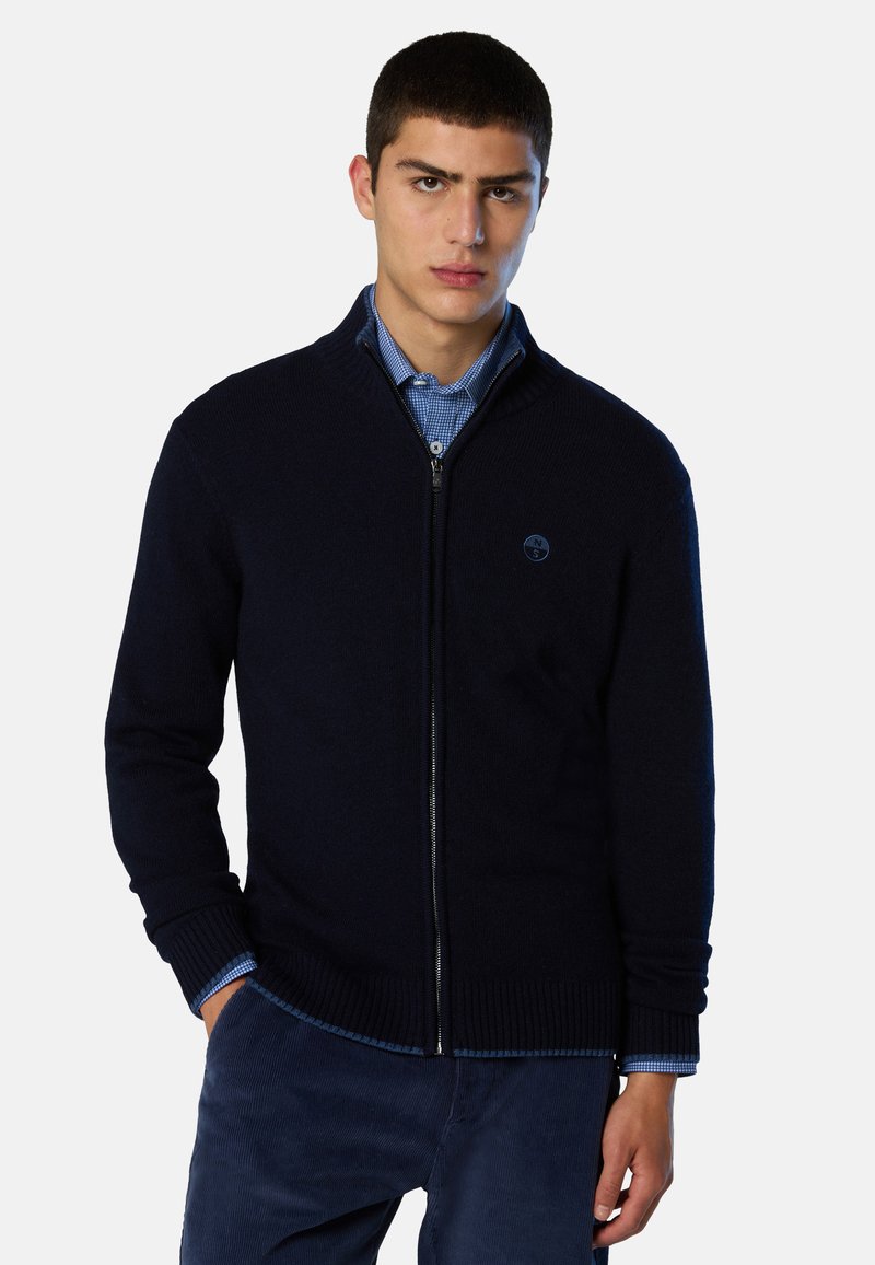 Maglione blu navy con cerniera, polsini e collo a costine, realizzato in morbido tessuto a maglia. Presenta un logo circolare sul lato sinistro del petto.
