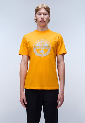 Lys orange bomulds T-shirt med rund halsudskæring og korte ærmer. Har et cirkulært gråt logografik på forsiden.