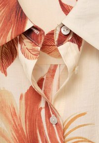 Short-sleeve floral shirt featuring a beige fabric with orange leaf patterns, a pointed collar, and white buttons on the placket.