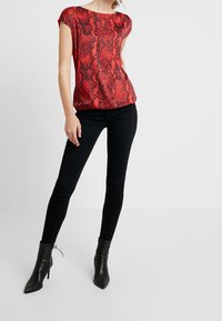 Haut à imprimé serpent rouge avec des manches courtes, un col rond et une coupe décontractée, associé à un jean skinny noir et des bottines noires à talons pointus.