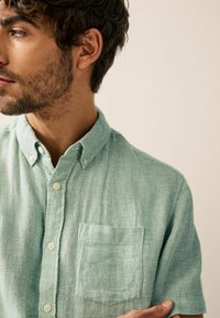 Light green short-sleeve button-up shirt with a textured fabric, featuring a chest pocket and classic collar details.