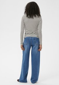 Gestreiftes Langarmhemd in Creme und Braun, kombiniert mit weit geschnittenen blauen Jeans, die Gesäßtaschen und eine strukturierte Denim-Oberfläche aufweisen.