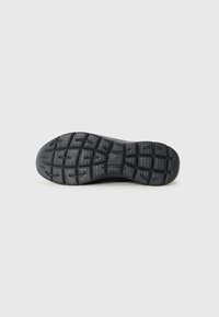Semelle de chaussure en caoutchouc noir avec un motif de grip texturé, dotée de rainures profondes pour l'adhérence et d'une finition lisse le long des bords.