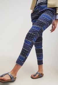 Blå byxor med mönster och olika motiv, i kortare längd och med elastisk midja. Matchas med mörkblå sandaler med tåskena.