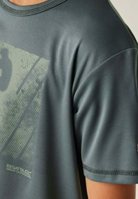 Camiseta atlética gris con tejido texturizado, cuello redondo, mangas cortas y un gran estampado gráfico en gris más claro en el frente.