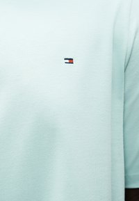 Ανοιχτό μπλε ύφασμα με ένα μικρό ορθογώνιο έμβλημα που διαθέτει μπλοκ χρωμάτων σε ναυτικό μπλε, άσπρο και κόκκινο κοντά στην περιοχή του στήθους.