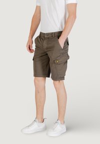 Pantaloni cargo khaki con tasche laterali, zip e passanti per cintura. Materiale in cotone con vestibilità comoda. Abbinati a sneakers bianche.