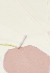 Cardigan crem cu o aplicație texturată roz în față. Material tricotat cu accente lila la manșete și margini. Două butoane vizibile.