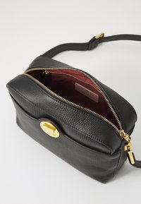 Black leather crossbody bag with a textured finish, gold zipper, and hardware. Red interior lining with one main compartment and a front flap.