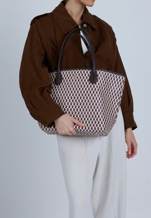 Geweven draagtas met een geometrisch patroon in tinten roze, crème en bordeaux, voorzien van twee donkerbruine leren handvatten en een stevig ontwerp.