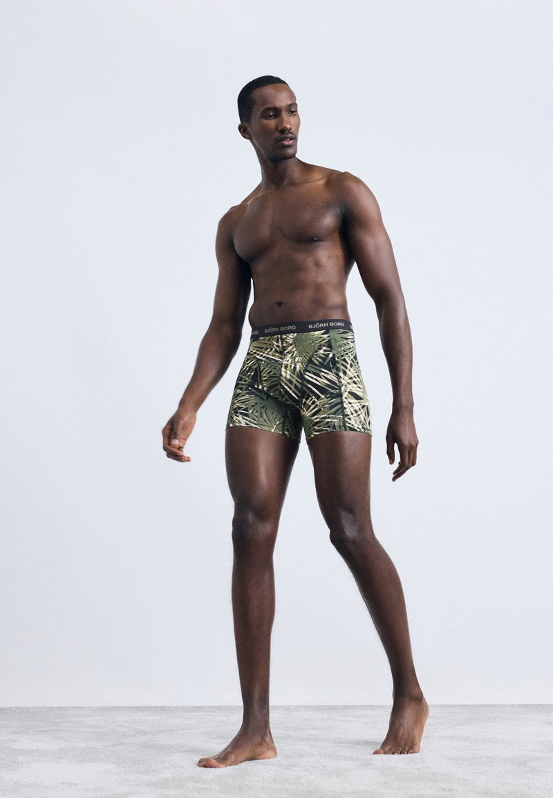 Zöld és fekete pálmalevél mintás boxeralsó, fekete derékrésszel, amelyen a "BJÖRN BORG" márkaneve található. Az anyag simának és rugalmasnak tűnik.