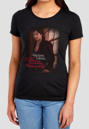 Woman wearing black t-shirt with a graphic of a man in dark clothing and text "The Vampire Diaries" and a red quote below.