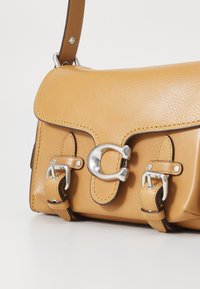 Borsa a spalla in pelle color tan con chiusura a patta magnetica e accessori in argento. Presenta due fibbie decorative con cinturini e cuciture a contrasto.