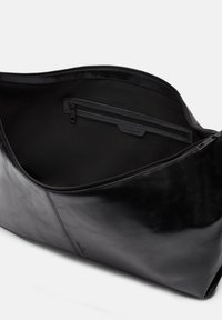 Czarna skórzana torba tote o gładkiej fakturze, z zamknięciem na zamek błyskawiczny u góry i wewnętrzną kieszenią. Minimalistyczny design z subtelnymi detalami marki.