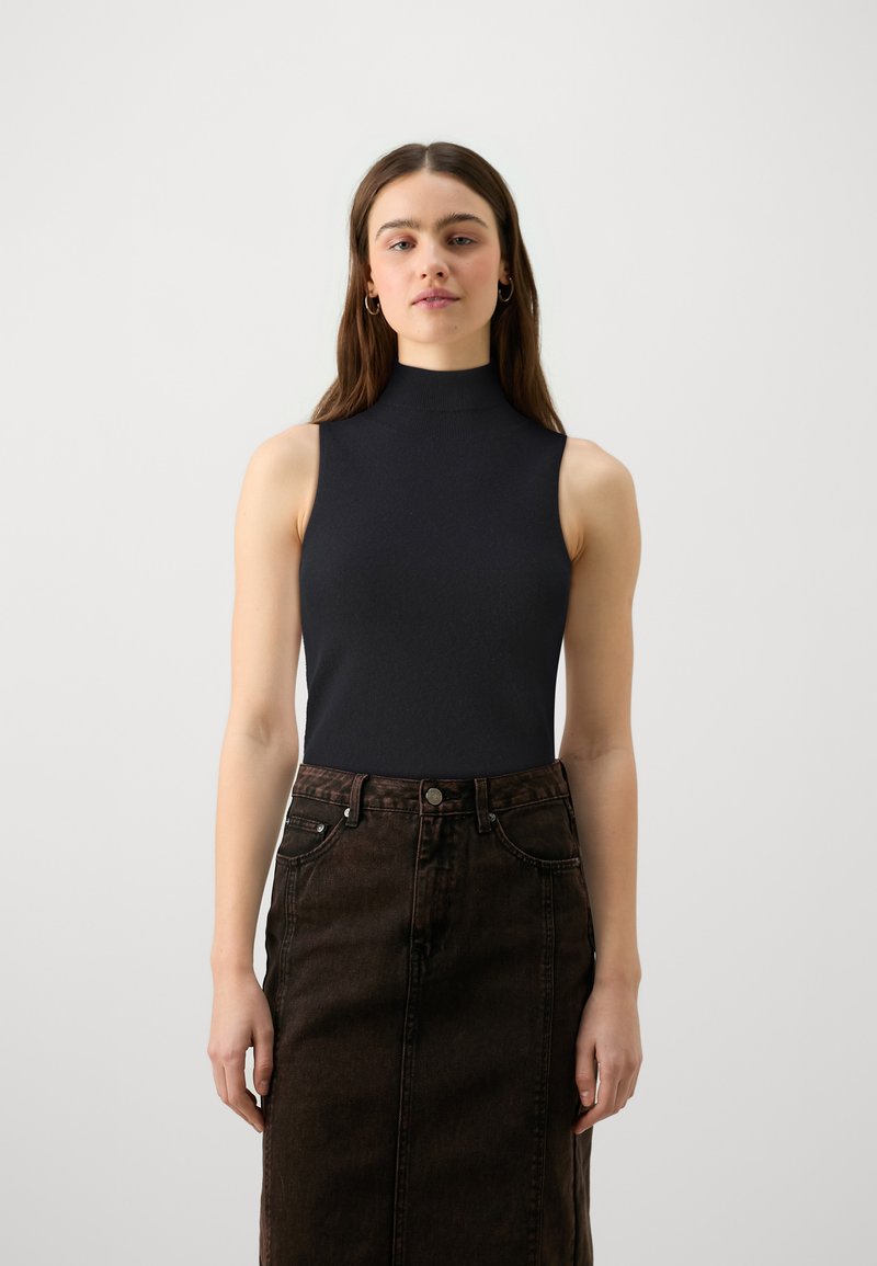 Schwarzes, ärmelloses Top mit hohem Kragen, kombiniert mit einem dunkelbraunen Jeans-Bleistiftrock. Die Stoffe sind glatt, eng anliegend und weisen dezente Strukturen auf.