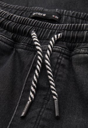Schwarze Jeansshorts mit elastischem Bund, ausgestattet mit einem weißen und schwarzen gestreiften Kordelzug und Metallakzenten.