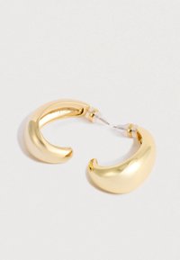 Une paire de boucles d'oreilles créoles en or poli, épais, en forme de croissant, avec des arrière-plans en plastique transparent sur un fond blanc.