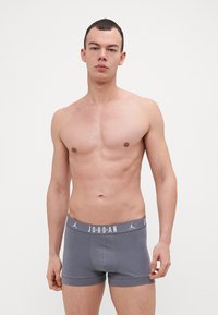 Grå boxershorts med en logobånd, der har en tætsiddende pasform og glat tekstur. Elastikken har "JORDAN" trykt i hvidt.