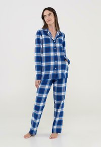 Conjunto de pijama a cuadros en azul y gris, con mangas largas, camisa abotonada y pantalones a juego, fabricado en un tejido suave. Botones blancos lisos detallan el frontal.