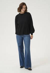 Black textured blouse with puffed sleeves and decorative stitching, paired with light blue flared jeans and black flats.