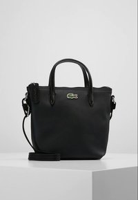 Fekete, texturált bőrből készült kézitáska két fogóval, levehető vállpánttal, és kis zöld krokodil logóval az elején.