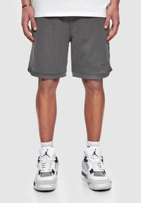 Shorts en mailles grises avec une texture légère et respirante, présentant un accent de logo. Associés à des baskets de sport blanches et noires.