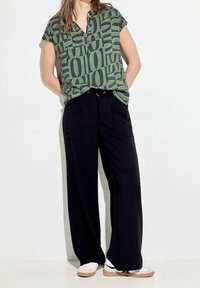 Blusa verde de manga corta con un estampado geométrico, combinada con pantalones de pierna ancha negros y zapatos blancos; tejido suave con un ajuste relajado.
