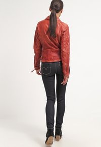 Red leather motorcycle jacket with textured finish, tapered design, and zipper accents, paired with dark skinny jeans and black ankle boots.