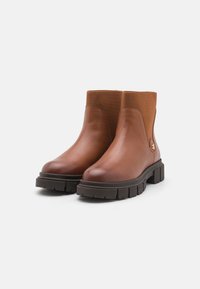Bottines en cuir marron avec panneaux élastiques sur les côtés, semelle en caoutchouc noire texturée et bout arrondi. Présente un accent en métal.