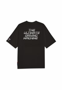 Sort t-shirt med fed, reflekterende tekst på ryggen, der står "DEN ULTIMATIVE KØREMASKINE." Logodetaljer på ærmerne.