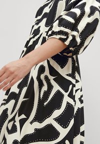 Robe à motif noir et blanc avec une coupe décontractée, des manches bouffantes et une taille froncée. Le tissu semble lisse avec un léger éclat.