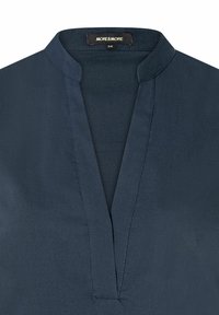 Marineblaue Bluse mit V-Ausschnitt, mit glatter Textur und dezenten Nähten. Etikett lautet "MORE & MORE," Größe 36.