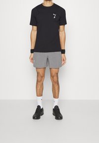 Svart atletisk tröja med korta ärmar, grå shorts, svarta skor och vita ankelsockor. Innehåller en logotyp på tröjan och shortsen.