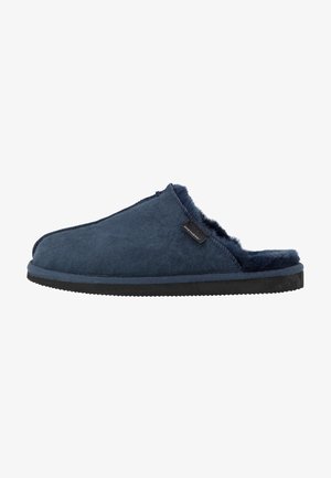 Pantofola in camoscio blu navy con rivestimento in pelliccia, design aperto sul retro e suola in gomma nera testurizzata. Presenta un piccolo etichetta con il marchio sulla parte superiore.