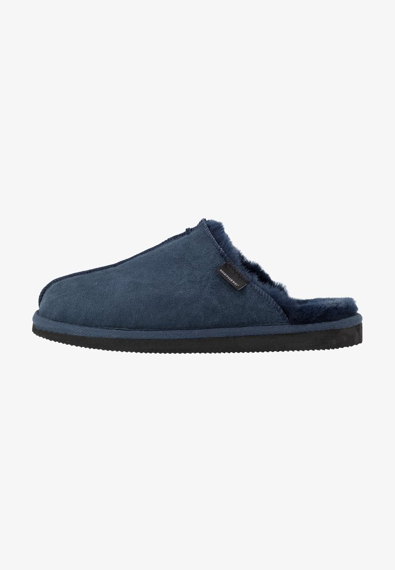 Navy blue suede slipper with fur lining, open back design, and a textured black rubber sole. Features a small branded tag on the upper.