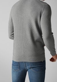 Suéter gris con un patrón de punto texturizado, cuello redondo y puños acanalados. Combinado con jeans azules, mostrando un ajuste casual desde la parte posterior.