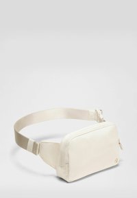 Riñonera compacta color blanco hueso con correa ajustable, cierre de cremallera y pequeño logo en la esquina frontal, mostrada sobre un fondo liso.