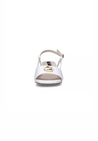 Sandalo slingback bianco in pelle con punta aperta, occhiello circolare dorato come accento sulla fascia e una soletta di colore neutro.