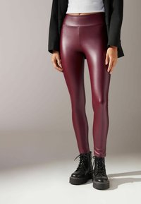 Leggings en simili cuir bordeaux avec une taille haute, une texture lisse et une coupe ajustée, associés à des bottes de combat noires à lacets.