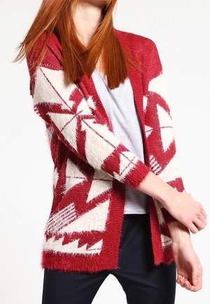 Cardigan rouge et blanc à motifs, confectionné en tricot pelucheux, présentant des designs géométriques et une ouverture sur le devant. Manches longues et coupe décontractée.