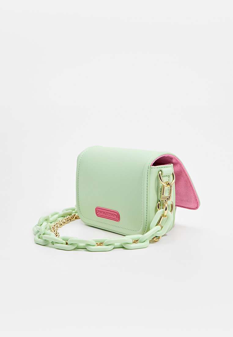Bolso de faux cuero verde menta con un interior rosa, forma rectangular, herrajes dorados y una correa de cadena gruesa. Presenta una placa con el logo en la parte frontal.