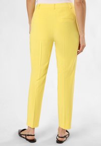 Pantalon jaune ajusté avec une texture lisse, présentant des jambes droites et des poches arrière discrètes. Porté avec des sandales plates noires.