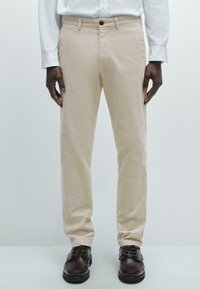 Beige cotton trousers with a straight leg design, featuring a button closure and side pockets, paired with brown lace-up shoes.