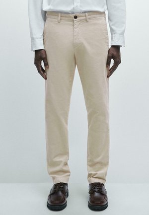 Beige cotton trousers with a straight leg design, featuring a button closure and side pockets, paired with brown lace-up shoes.