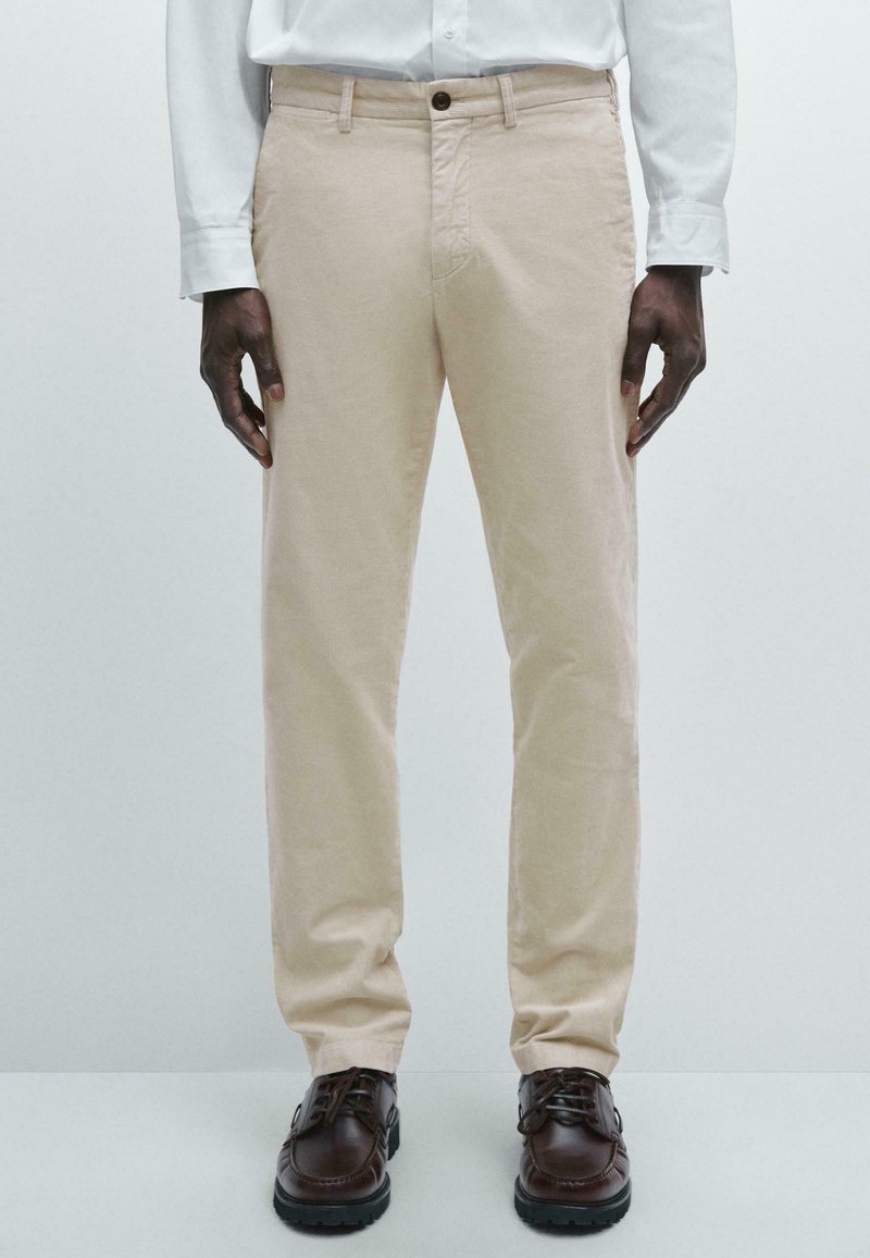 Beige cotton trousers with a straight leg design, featuring a button closure and side pockets, paired with brown lace-up shoes.