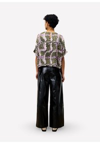 Losse blouse met een kleurrijk, gemusterd ontwerp in tinten groen, roze en zwart; gecombineerd met hoge, glanzende zwarte leren broek.